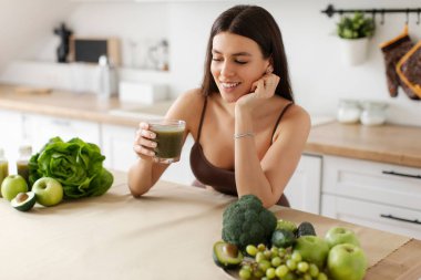 Slim mutlu bayan detoks smoothie içiyor, modern mutfakta sağlıklı içkinin tadını çıkarıyor. Kilo kaybı için besin