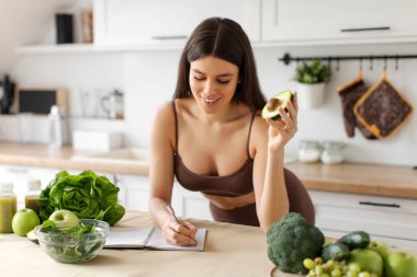 Kilo verme diyet planı. Defterine sağlıklı yemek tarifleri yazan bir kadın, mutfak masasında günlük yemek planlaması, bedava yer.