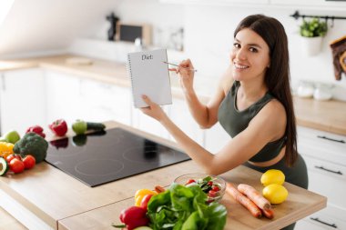 Sağlıklı menü ve kilo verme tarifleri yazarken diyet planıyla poz veren gülümseyen bayan, boş yer. Zayıflama beslenme kavramı