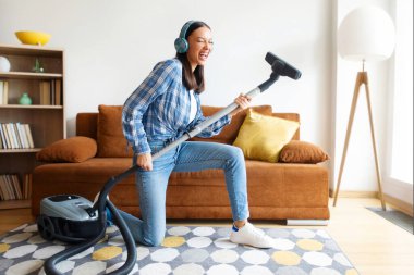 Temizlik eğlencelidir. Neşeli bir kadın, evini süpürürken kulaklıkla müzik dinliyor, süpürgeyi gitar olarak kullanıyor, ev işlerini yapmaktan hoşlanan bir kadın.