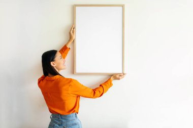 Evin içinde duran beyaz duvara resim asan bir kadın. İç mimari için modern sanat ve dekor