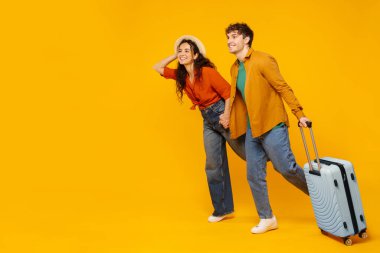 Seyahat ilanı. Heyecanlı çift bavulla koşuyor ve sarı arka planda fotokopi alanına bakıyor. Tatile çıkmaya hazır, tam boy.