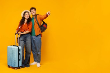 Heyecanlı Avrupalı çift tatile çıkıyor, sırt çantası, bavul, fotokopi alanına bakıyor, harika seyahat teklifleri sunuyor, sarı arka plan