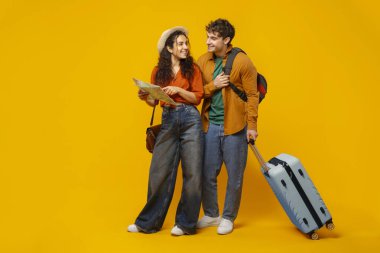 Mutlu adam ve kadın turist haritası ve planlama tatili kullanıyor, sarı arka planda bavulla duruyor, uzun bir çekim.