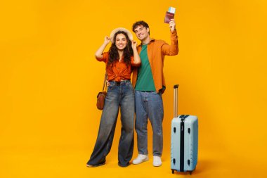 Mutlu eşler tatile hazır, kadın ve erkek bavul, pasaport ve biletler sarı arka planda, tam boy