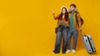 Sarı arka planda duran valizli mutlu çift gezginleri, haritayı tutan ve boş alana bakan kadını, panorama