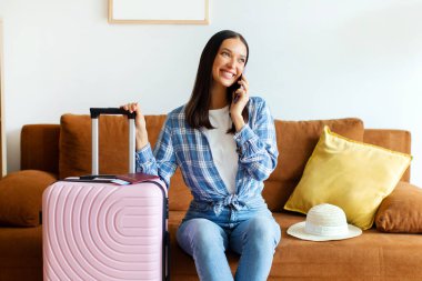 Heyecanlı bayan gezgin cep telefonuyla konuşuyor, bavuluyla koltukta oturuyor, havaalanına taksi çağırıp,