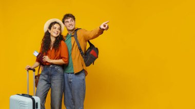 Sıcak turlar. Boş alanı gösteren bavulu olan çift, seyahat teklifi veya reklam için sarı arkaplanda kopya alanı gösteriyor, panorama