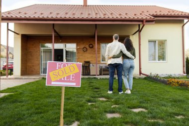 Satın alma, emlak konsepti. Arka planda kucaklaşan çiftlerin kendi evlerine baktığı 
