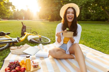 Heyecanlı bayan sağlıklı yemekten hoşlanıyor, salata yiyor, yaz vakti parkta piknik yapıyor, dışarıda dinleniyor ve dinleniyor.