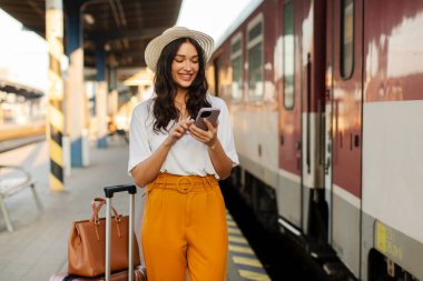 Tren peronunda dururken akıllı telefonunu kullanan genç bir gezgin. İnsanlar ve ulaşım kavramı