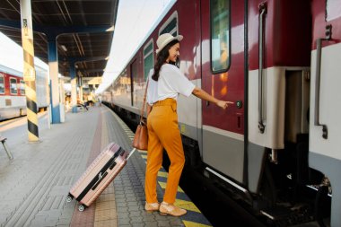 Kadın turist girmek için tren kapısında düğmeye basıyor, bavulla ayakta duruyor, hafta sonu tatiline hazır, tam boy. Demiryolu konsepti