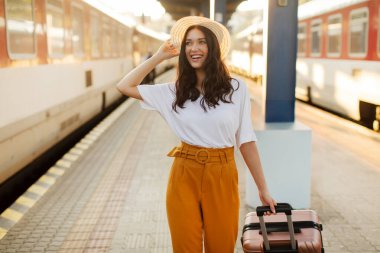 Gülümseyen Avrupalı kadın yolcu bavuluyla tren istasyonunda bekliyor, bayan hafta sonu gezisine hazır.