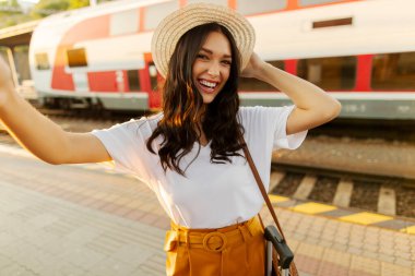 Avrupalı turist, tren istasyonunda arka planda lokomotife karşı durarak selfie çekiyor.