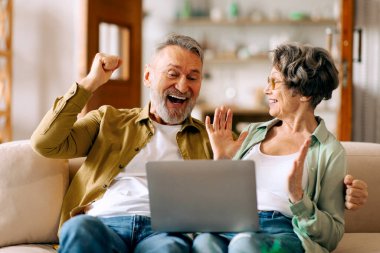 Heyecanlı yaşlı eşler yumruklarını sıkarak kazananlara jest yapıyor. Koltukta dizüstü bilgisayarla oturuyor, e-posta okuyor, harika haberleri kutluyor.