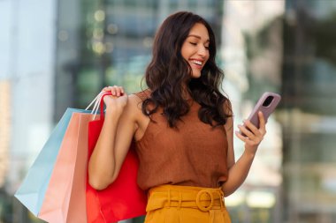 Alışveriş poşetleriyle, dışarıda alışveriş merkezinin yanında duran akıllı telefondan yazı yazan modaya uygun bir bayan, boş yer. Büyük indirim, mağazadan teklif.