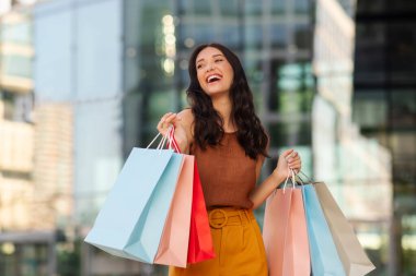 Elinde kağıt poşetler olan heyecanlı bir bayan, açık havada alışveriş merkezinin önünde duran bir reklam teklifi. Harika satış konsepti