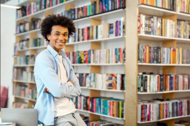 Kitap raflarının önünde kütüphanede duran zeki Afro-Amerikan öğrenci, okumaktan mutlu, boş alan.
