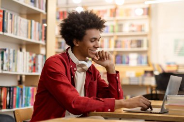 Bilgisayarı online kütüphane dersi için kullanan mutlu, zeki siyah öğrenci, eğitime modern bir yaklaşım ve boş alan gösteriyor.