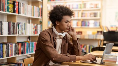 Kütüphanede dizüstü bilgisayarla okuyan, kitaplıkların arasında masa başında oturan zeki, siyah bir öğrenci. Eğitim kavramı