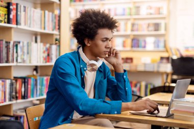 Kütüphanede dizüstü bilgisayarla okuyan, kitaplıkların arasında masa başında oturan zeki, siyah bir öğrenci. Eğitim kavramı