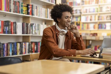 Kolej kütüphanesinde dizüstü bilgisayar kullanan Afro-Amerikan bir öğrenci. İnternette çalışıyor ya da test alanına hazırlanıyor. Teknoloji güdümlü akademik çabalar