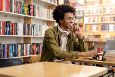 Kolej kütüphanesinde dizüstü bilgisayar kullanan Afro-Amerikan bir öğrenci. İnternette çalışıyor ya da test alanına hazırlanıyor. Teknoloji güdümlü akademik çabalar