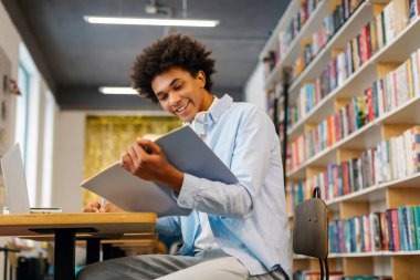 Kütüphanede okuyan, kitap okurken notlar yazan, derslere hazırlanan, boş alan olan mutlu zenci öğrenci.