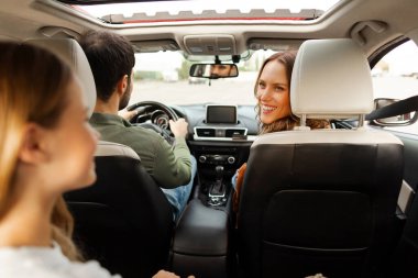 Mutlu ebeveynler ve kızlar araba yolculuğunda arabada oturuyorlar, kadın çocuk kızına dönüyor ve konuşuyor, dikiz aynasından.