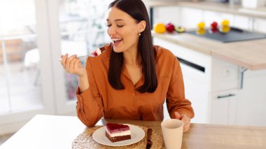 Genç bayan sıcak kahveyle pasta yemekten, modern mutfakta oturmaktan, sağlıksız kahvaltı yapmaktan ya da atıştırmaktan hoşlanır.