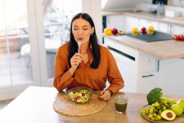 Evdeki mutfakta sebze salatası yiyen tatmin olmuş genç bir kadın, fotokopi odası. Vejetaryenlik, sağlıklı beslenme ve sağIık kavramı
