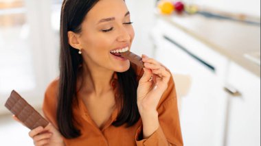 Çikolata yiyen tatmin olmuş genç bir bayan. Evde lezzetli tatlı yiyor. Yakın plan. Sağlıksız beslenme, aldatma yemek konsepti