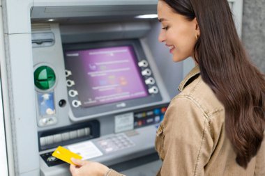 ATM kullanan, kredi kartı kullanan, karttan para çeken ve dışarıda para transferleri yapan bir kadın.