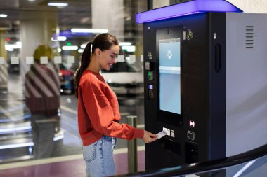 Alışveriş merkezinin yeraltı otoparkında park cezası ödeyen kadın.
