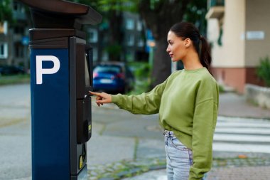 Park ücretini ödeyen genç bir kadın, açık hava elektronik ödeme terminalini kullanan bir bayan sürücü, park ücretini bitirmek için otomatik sokak büfesini kullanan bir kadın.