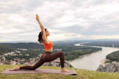 Dağın tepesinde şehir manzarasına karşı yoga yapan sağlıklı, fit bir kadın sabah sporu, yan görüş ve boş alan için zaman harcıyor.