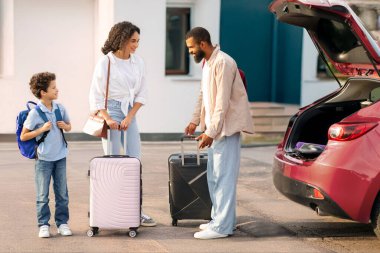 Aile tatile çıkıyor. Baba, bavullarını arabaya koyar, anne ve oğlu otomobilin yanında durur, tam yol ileri.