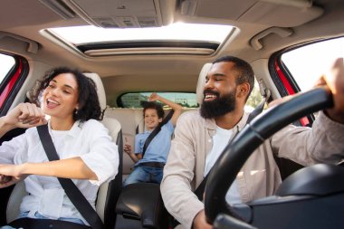 Oğlu olan eğlenceli bir Latin ailesi arabayla bir yerlere giderken, arabada şarkı söyleyip dans ediyorlar.