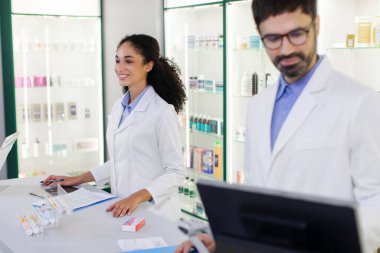 Kasanın arkasında duran kadın ve erkek eczacılar eczanede sağlık ürünleriyle çalışan tıbbi profesyoneller.