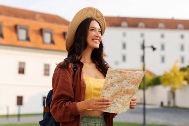 Gülümseyen kadın tarihi binanın önünde elinde açık bir haritayla duruyor ve simgeye hayran, şapka ve sırt çantası takan bayan turist.