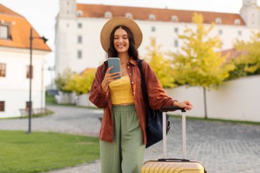 Sırt çantalı ve bavullu mutlu bir kadın yalnız seyahat ediyor, Avrupa 'da yürüyor ve akıllı telefonda GPS navigatörü kullanıyor.
