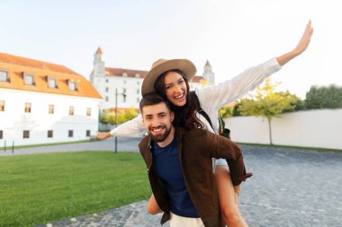 Neşeli bir adam, kasabada yürürken ve tatillerinin tadını çıkarırken keyifli kız arkadaşını sırtında taşır.