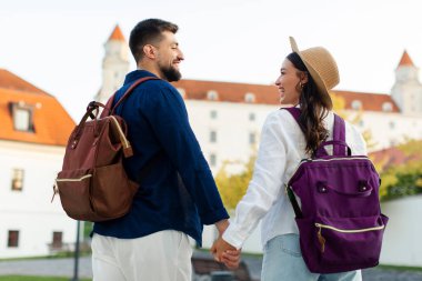 Mutlu gezginler şehirde gezmekten zevk alıyorlar, sırt çantaları takıyorlar, el ele tutuşuyorlar ve birbirlerine gülümsüyorlar.