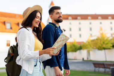 Genç mutlu çift eski şehirde yürüyor, kadın haritaya bakıyor ve şehir simgelerine giden yolları arıyor yaz gezisinin tadını çıkarırken, bedava uzay