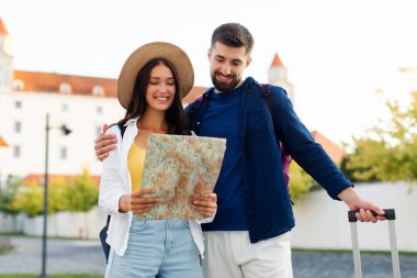 Avrupa şehir caddesinde seyahat valizleriyle yürüyen ve şehir haritasına bakan mutlu Avrupalı iki turist
