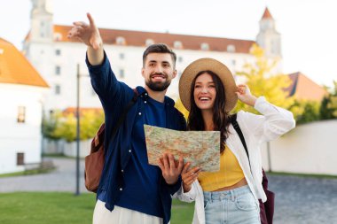 Mutlu çift balayı seyahatlerinin tadını çıkarıyor, haritayı şehir işaretlerini aramak için kullanıyor, adam işaret ediyor.