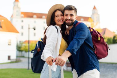 Mutlu gezginler şehirde sarılıp balayının tadını çıkarıyorlar. Sırt çantaları ve bavullarıyla eski bir kasabada poz veriyorlar.