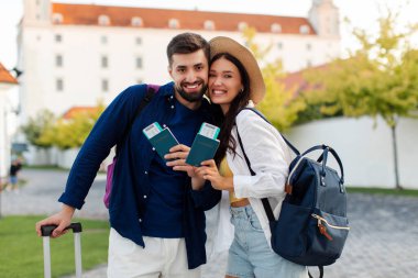 Pasaportları ve biletleri olan mutlu Avrupalı bir adam ve kadın şehirde yürüyor ve kameraya poz veriyor.