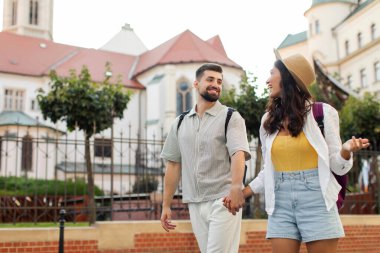 Güzel Avrupa şehrinde sokakta yürürken el ele tutuşurken ve mutluluğu ifade ederken mutlu genç adam ve kadın konuşuyorlar.