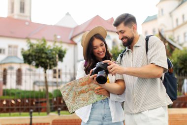 Mutlu çift şehri keşfederken gezmekten zevk alıyor, kadın kasabada yürürken harita tutuyor ve adam kamerada fotoğraf çekiyor.